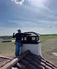A Premium Chimneys technician on a tile roof beside a newly installed chimney cap