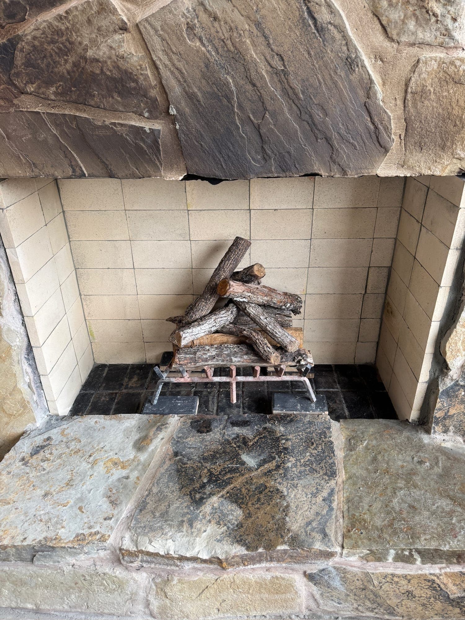 Split hardwood logs stacked on a metal grate inside a tile lined fireplace firebox